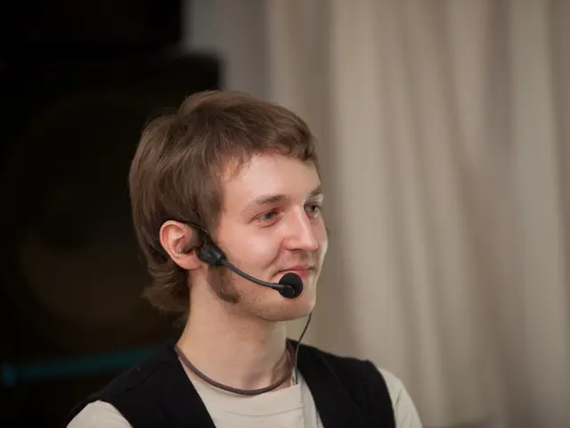 In this image there is a man with cream t-shirt and microphone. At the back there is a curtain. On...