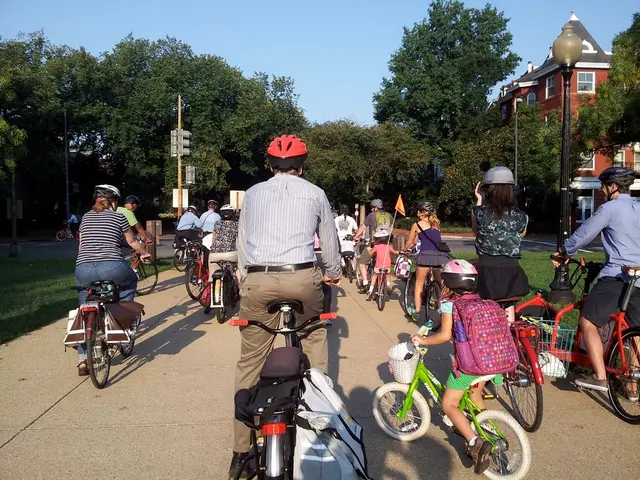 Few people are riding their bicycles on a road there are trees at here and houses in the right and...