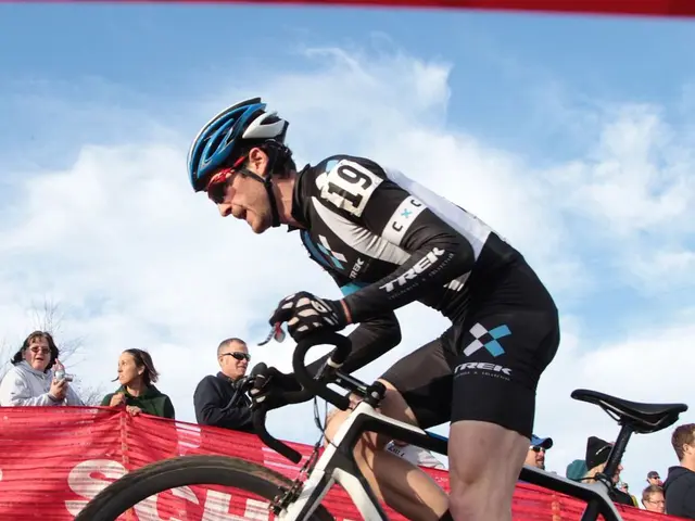 In this image there is a man cycling, in the background there is a banner, on that banner there is...