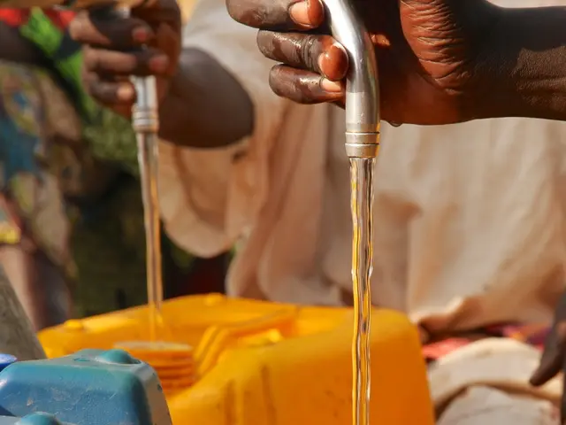 In this image there are hands of two people holding pipes. There is the liquid flowing from the...