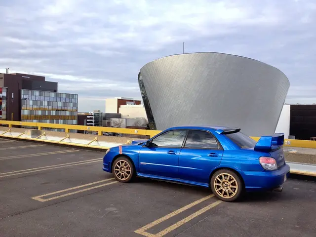 In this picture there is a blue color car in the center of the image, on the road and there are...