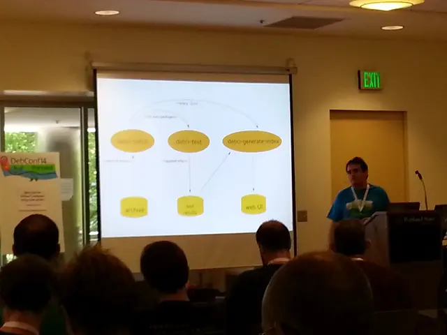 In this image we can see few persons are sitting on the chairs, a person is standing, and here is...